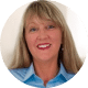 Smiling woman with long blonde hair wearing a light blue shirt, posed against a light background.